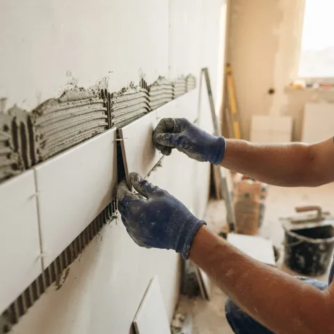 Mains gantées posant des carreaux de plâtre sur un mortier adhésif
